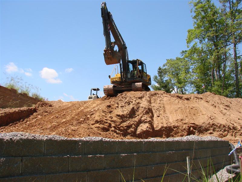 Excavator preparing to backfill a retaining wall