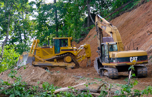 This bulldozer and  excavator are working together grading a slope for a road on steep terrain.